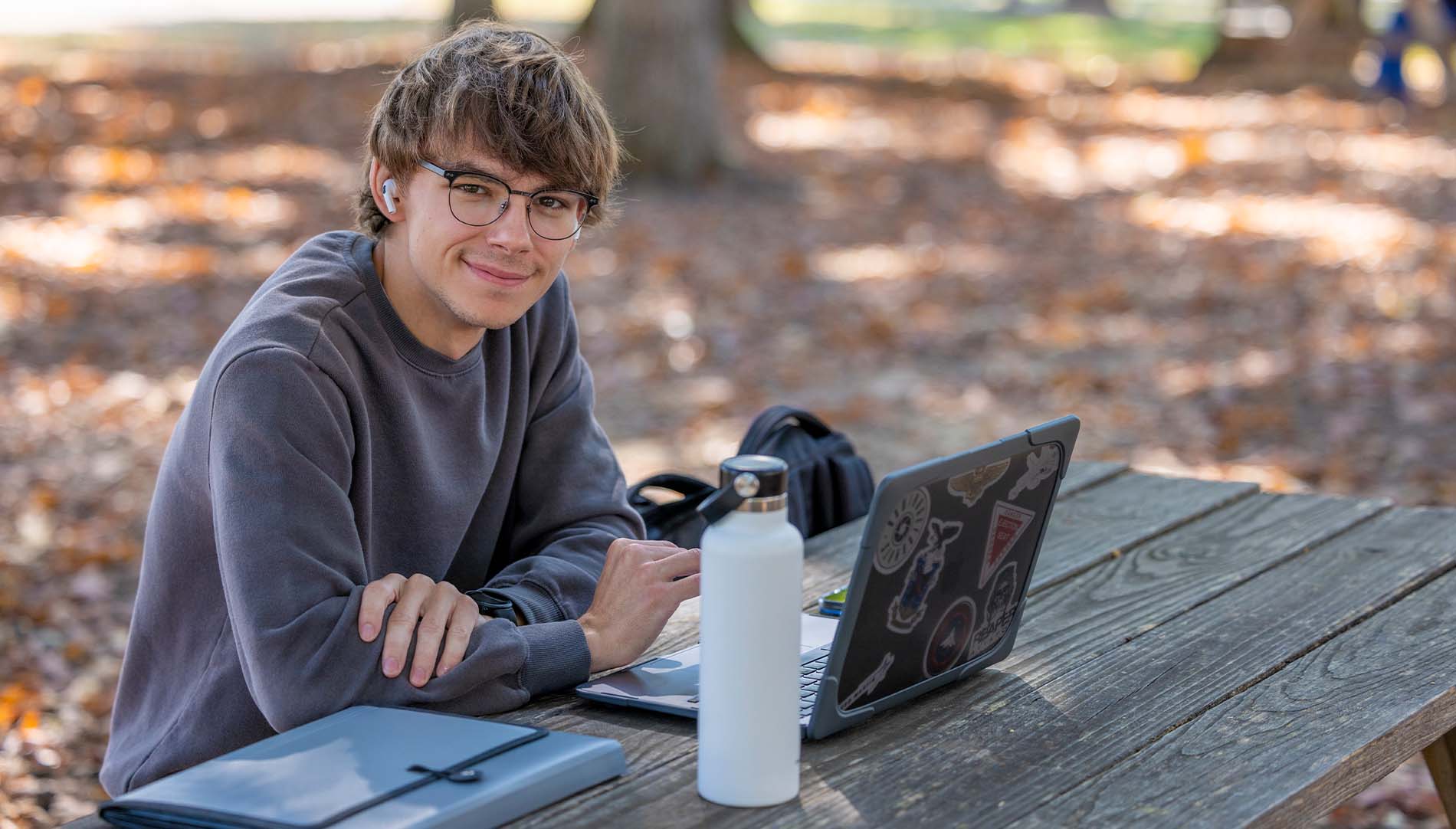 student sitting outdoors with a laptop